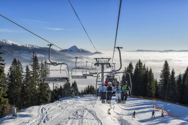 Bulutların üstünde telesiyej üzerinde yükselen kayakçı