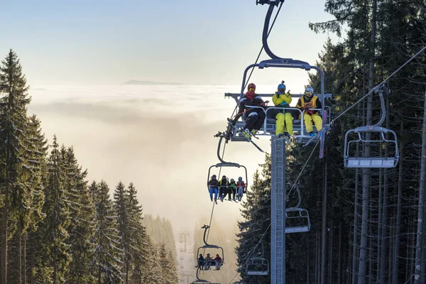 Happy skiers on chairlift above the clouds — Stock Photo, Image