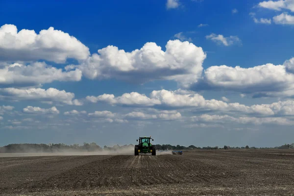Groene trekker het cultiveren van een veld met blauwe lucht en de wolken op th — Stockfoto