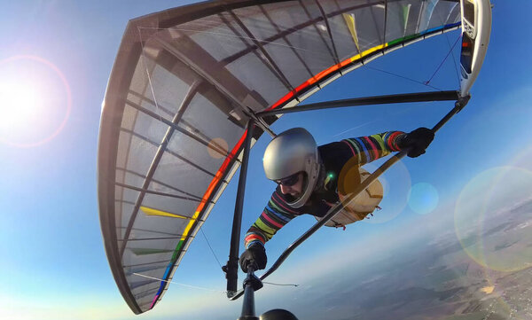 Hang glider pilot on colorful wing makes photo selfie high above ground. Concept of self isolation and social distancing activity. Extreme sport outdoors.