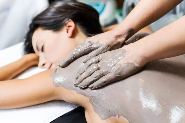 Beautiful young woman having clay body mask apply by beautician. — Stock Photo, Image