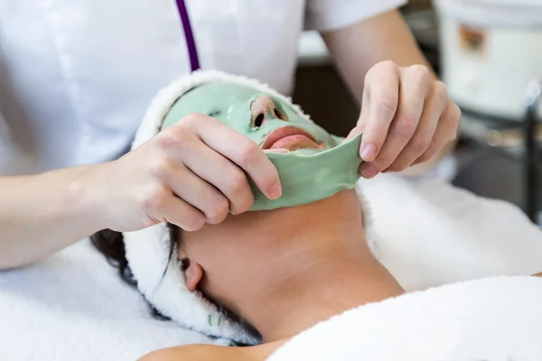 Hermosa joven con máscara facial antienvejecimiento en el spa . — Foto de Stock