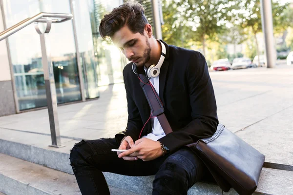 Knappe jongeman met behulp van zijn mobiele telefoon in de straat. — Stockfoto