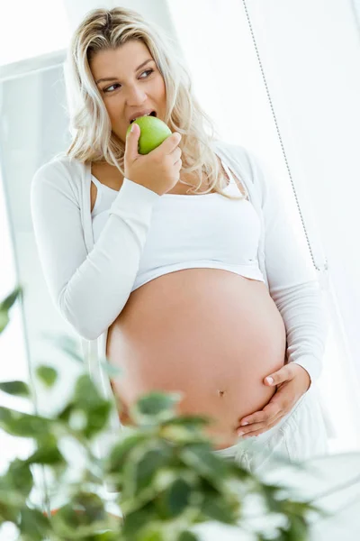 美しい妊娠中の女性家でリンゴを食べる. — ストック写真