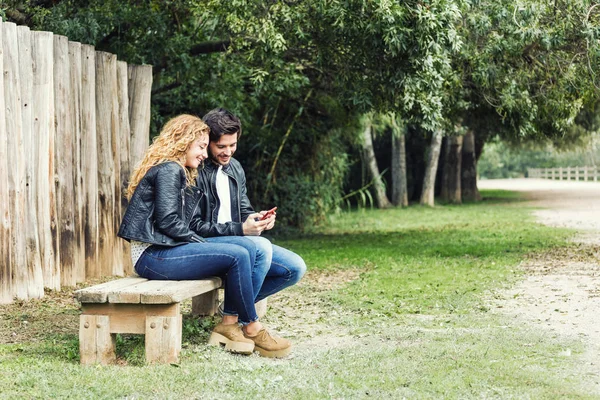 Beautiful young couple using they mobile phone in the park. — Stock Photo, Image