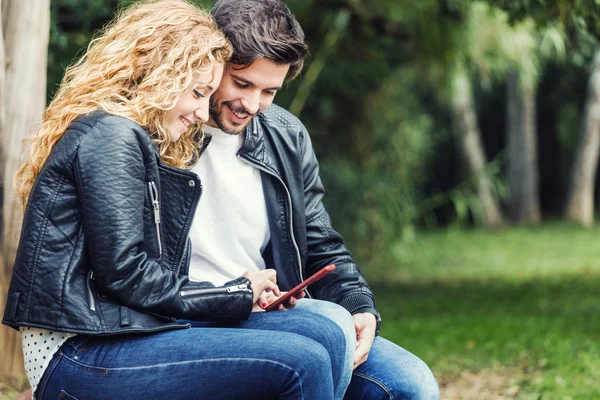 Hermosa pareja joven utilizando el teléfono móvil en el parque . —  Fotos de Stock