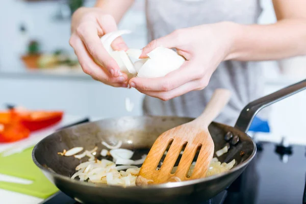 Mladá žena smažení cibule do pánvičky v kuchyni. — Stock fotografie
