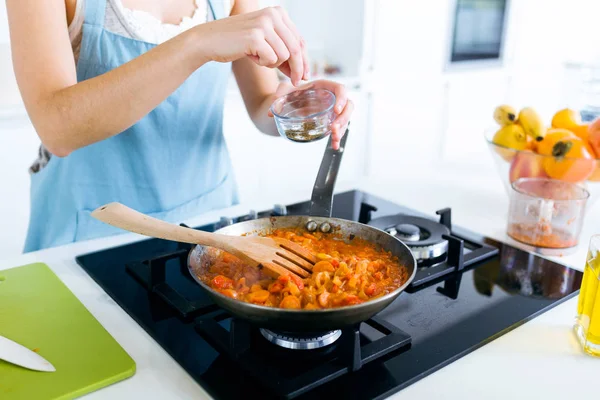 Молода жінка додає перець і змішує їжу на сковороді . — стокове фото