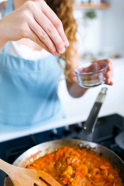 Jonge vrouw peper toevoegen en mengen van voedsel in koekenpan. — Stockfoto