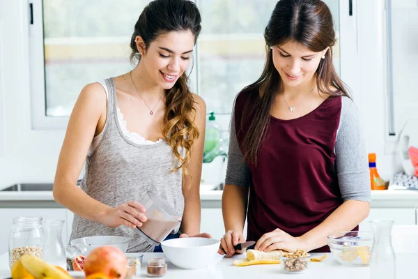 Twee mooie jonge vrouwen voorbereiding van graan kommen in de keuken. — Stockfoto