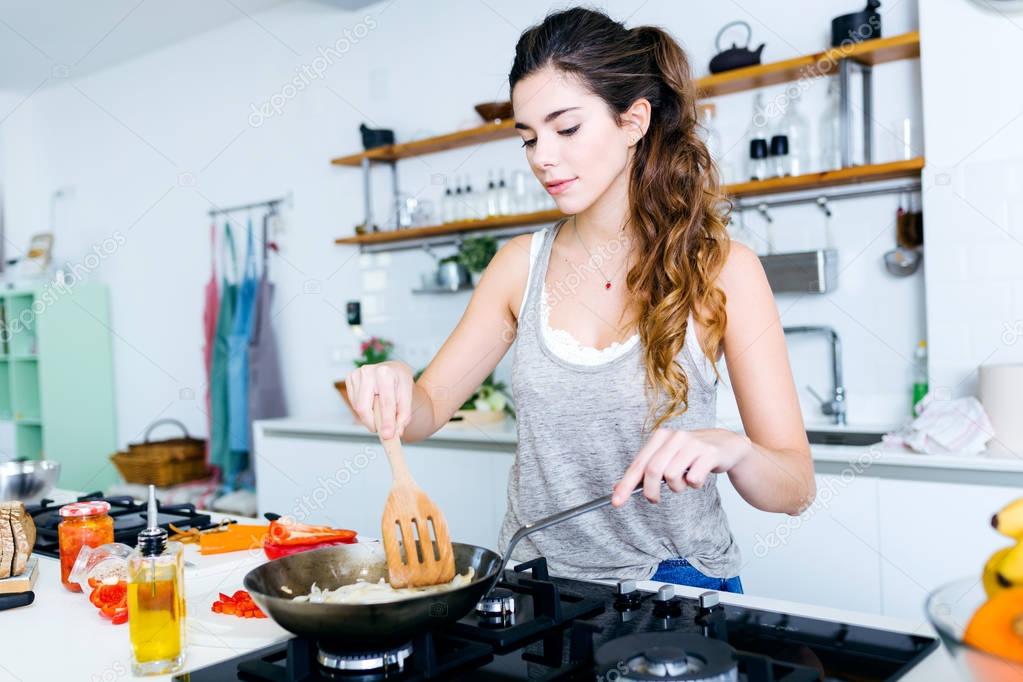 Young woman frying onion into the pan in the kitchen.
