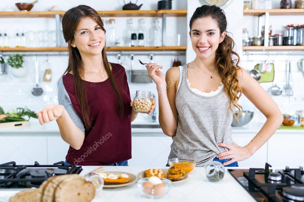 Two beautiful women preparing toasts with mashed vegetables, eggs and seeds.
