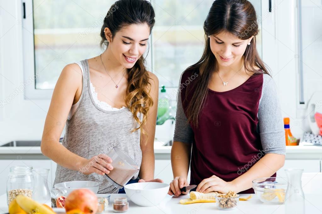 Two beautiful young women preparing cereal bowls in the kitchen.