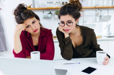 İki genç kadın mutfakta kahve yudumlarken laptop ile çalışma.