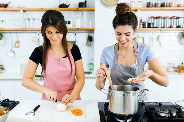 Twee mooie vrouwen snijden en koken van verse groenten in de keuken. — Stockfoto