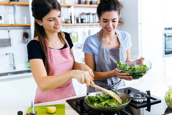 Two beautiful young women frying chards into the pan. — Stock Photo, Image