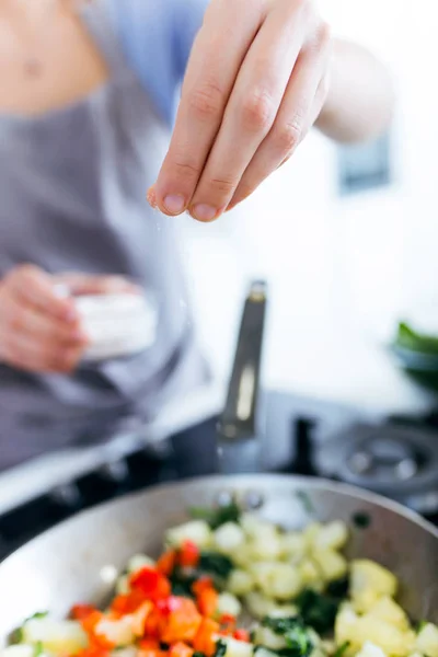 Рука молодой женщины, добавляющей соль в кастрюлю . — стоковое фото