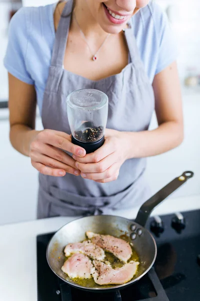 Young woman adding pepper to chicken into the pan. — Stock Photo, Image