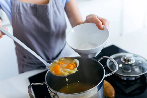 Young woman serving vegetable soup in the kitchen. — Stock Photo, Image