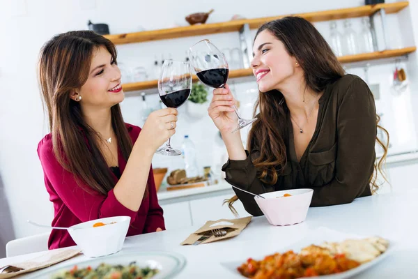 Två vackra unga kvinnor dricker vin några medan man äter i köket. — Stockfoto