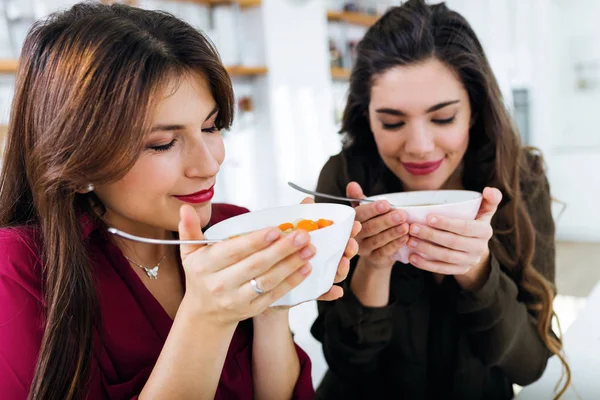 Twee mooie jonge vrouwen eten van groenten soep in de keuken. — Stockfoto