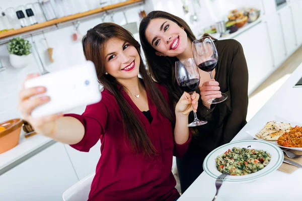 Zwei junge Frauen mit Mobiltelefon beim Essen in der Küche. — Stockfoto