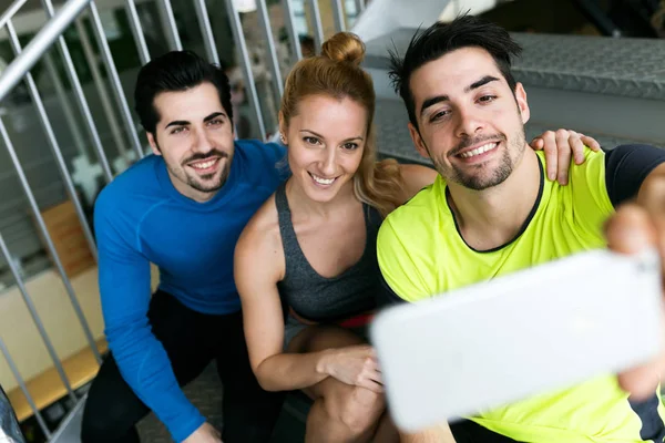 Grupo de deportistas que utilizan teléfono móvil en el gimnasio . —  Fotos de Stock