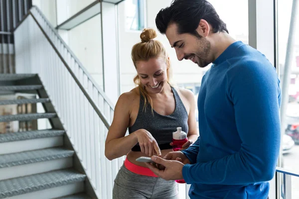 Deportiva pareja joven utilizando el teléfono móvil en el gimnasio . — Foto de Stock