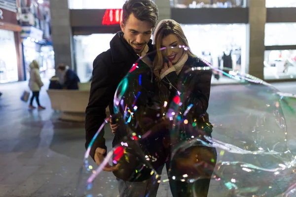 Hermosa pareja joven mirando grandes burbujas de jabón en la calle — Foto de Stock
