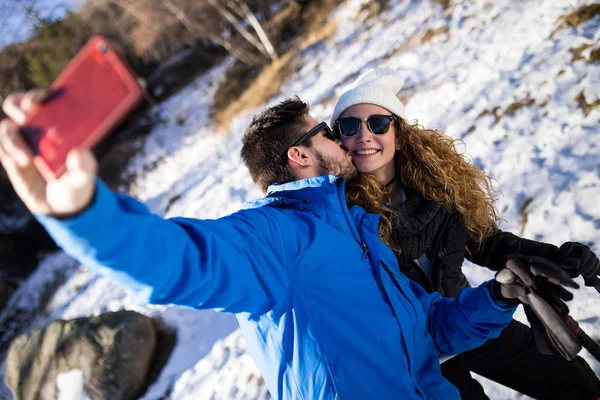 Mutlu çift kış arkaplanı boyunca akıllı telefonuyla selfie çekiyor.. — Stok fotoğraf