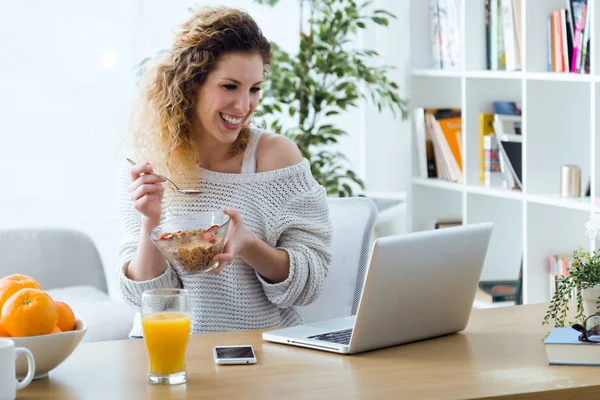 Schöne junge Frau arbeitet mit Laptop, während zu Hause gegessen wird. — Stockfoto