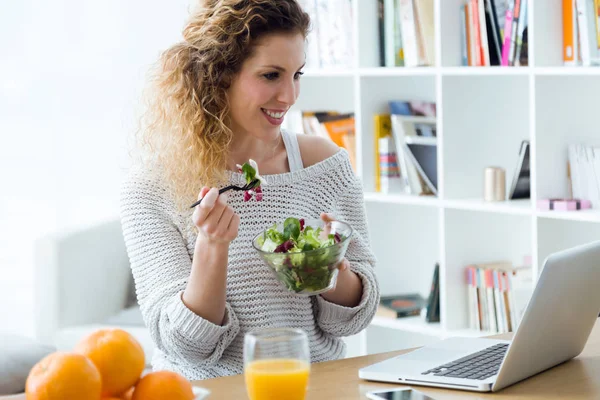 Mulher bonita trabalhando com laptop enquanto come em casa . — Fotografia de Stock