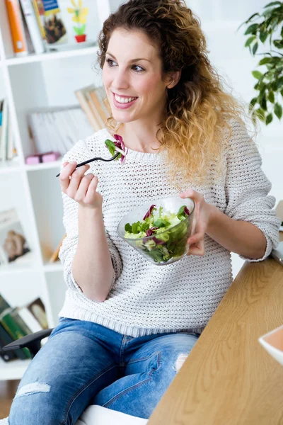 Vacker ung kvinna äter sallad hemma. — Stockfoto