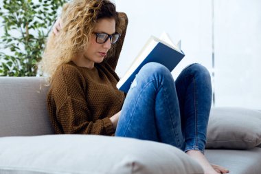 Güzel genç bir kadın evde kitap okuyor..