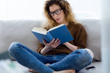 Güzel genç bir kadın evde kitap okuyor..