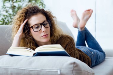 Güzel genç bir kadın evde kitap okuyor..