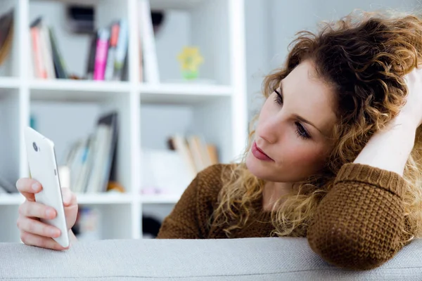 Belle jeune femme utilisant son téléphone portable à la maison . — Photo