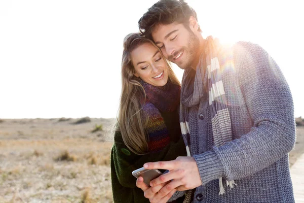 Schönes junges Paar mit Handy in einem kalten Winter am Strand. — Stockfoto