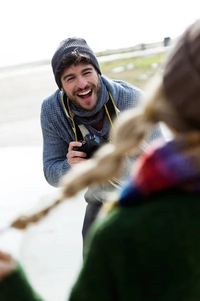 Happy young couple taking photos with camera in a cold winter on the beach. — Stock Photo, Image