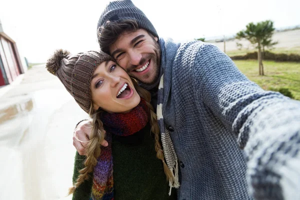 Vackra unga par med hjälp av mobiltelefon i en kall vinter på stranden. — Stockfoto
