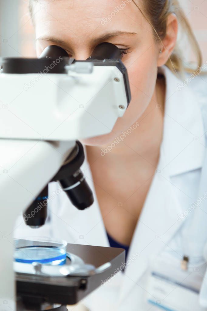 Young woman looking through microscope in laboratory.