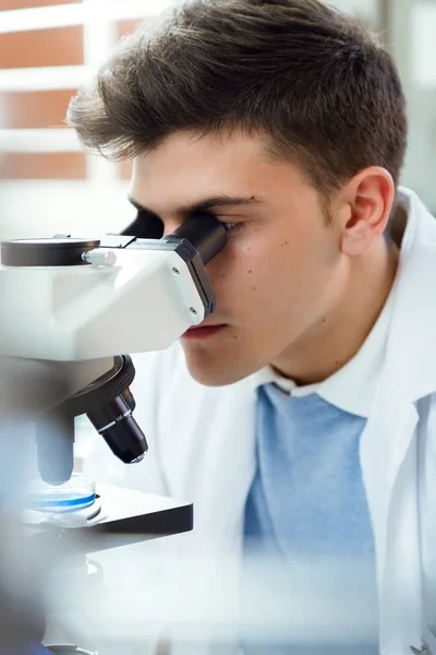 Ung man tittar genom mikroskopet i laboratorium. — Stockfoto