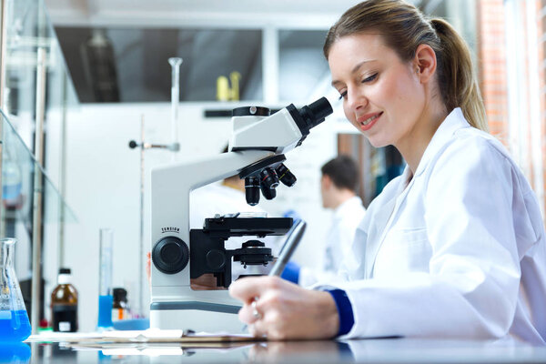Young woman looking through microscope in laboratory.