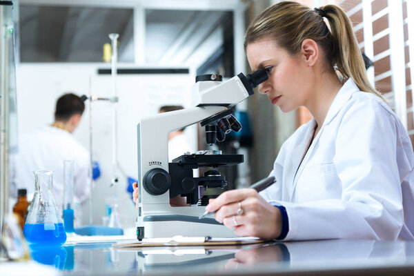 Young woman looking through microscope in laboratory.