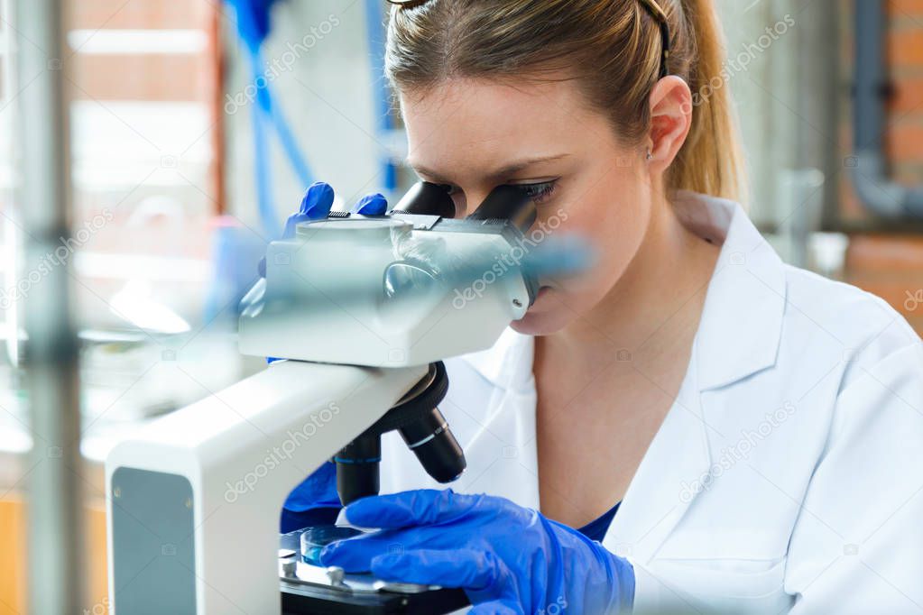 Young woman looking through microscope in laboratory.