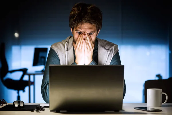 Csinos, fiatal férfi éjjel laptop az irodájában dolgozik. — Stock Fotó