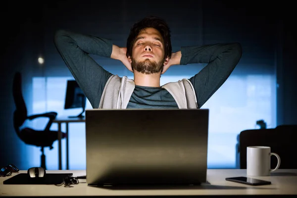 Csinos, fiatal férfi éjjel laptop az irodájában dolgozik. — Stock Fotó