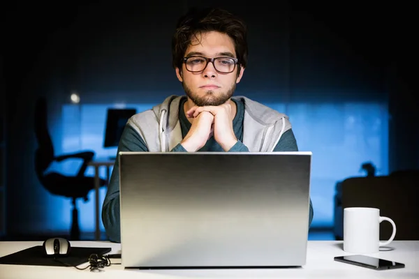 英俊的年轻男子，夜间与笔记本电脑在他的办公室工作. — 图库照片