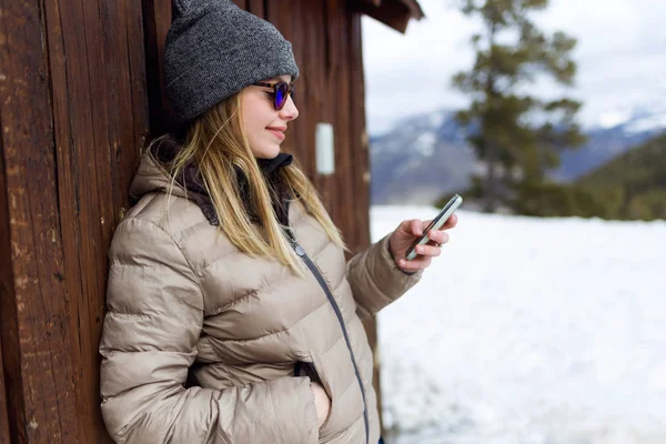 Όμορφη νεαρή γυναίκα που χρησιμοποιεί το κινητό της τηλέφωνο πέρα από το υπόβαθρο του χειμώνα. — Φωτογραφία Αρχείου