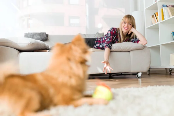 Hermosa joven con su perro jugando con la pelota en casa . — Foto de Stock